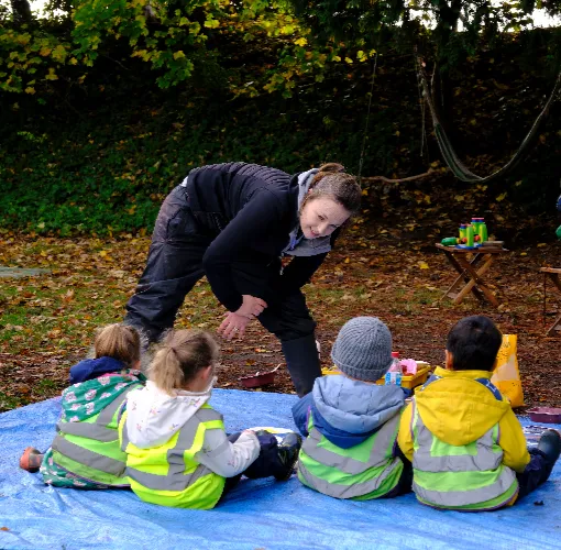 children sat on mat in garden looking at teacher